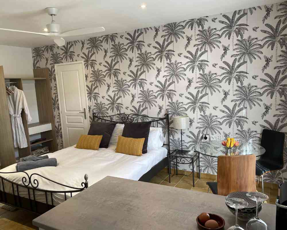 Studio bedroom at Château de la Boutinière with double bed, palm-print wallpaper, small dining table and kitchenette