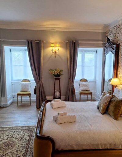 Bedroom at Château de la Boutinière with double bed, fireplace, armchairs and tall windows with curtains