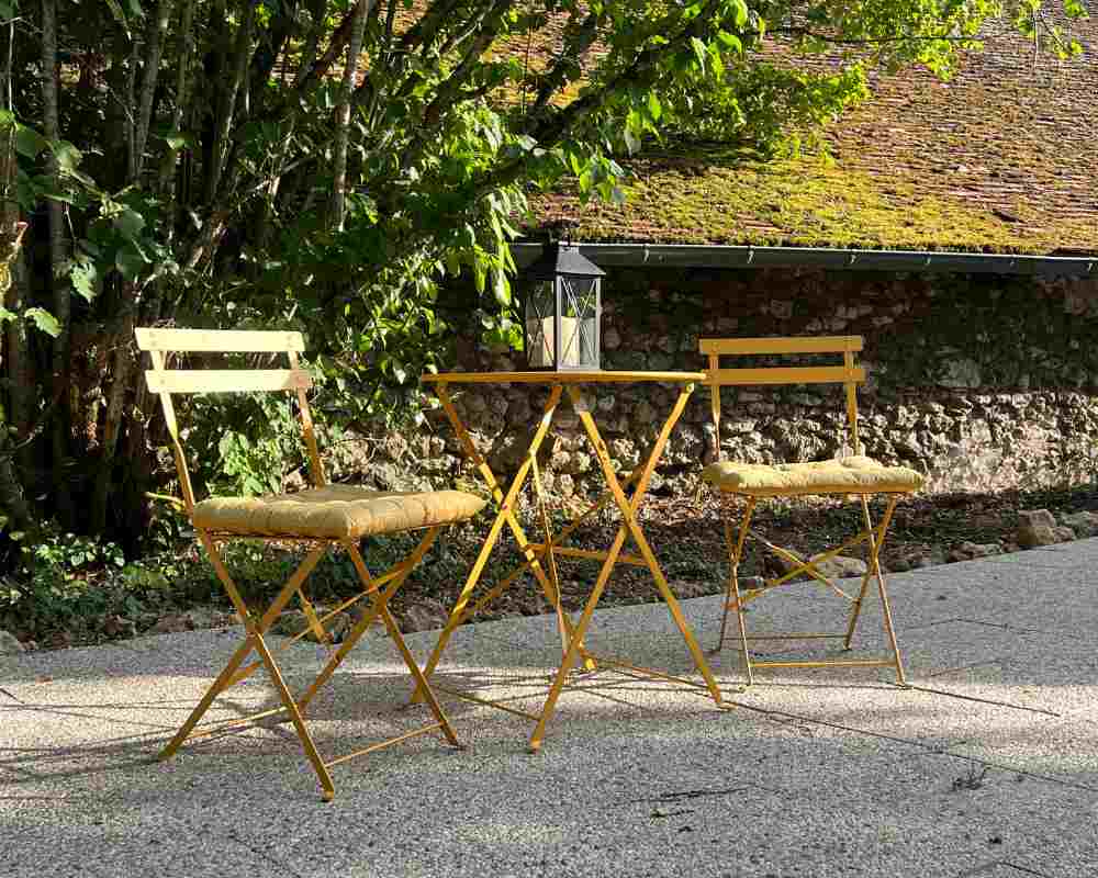 Outdoor bistro table with two folding chairs set beside a stone wall and trees at Château de la Boutinière