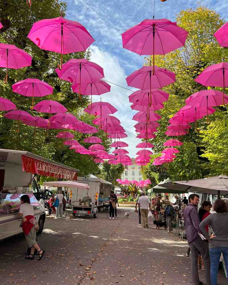 Village market street with stalls and bright pink umbrellas hanging overhead