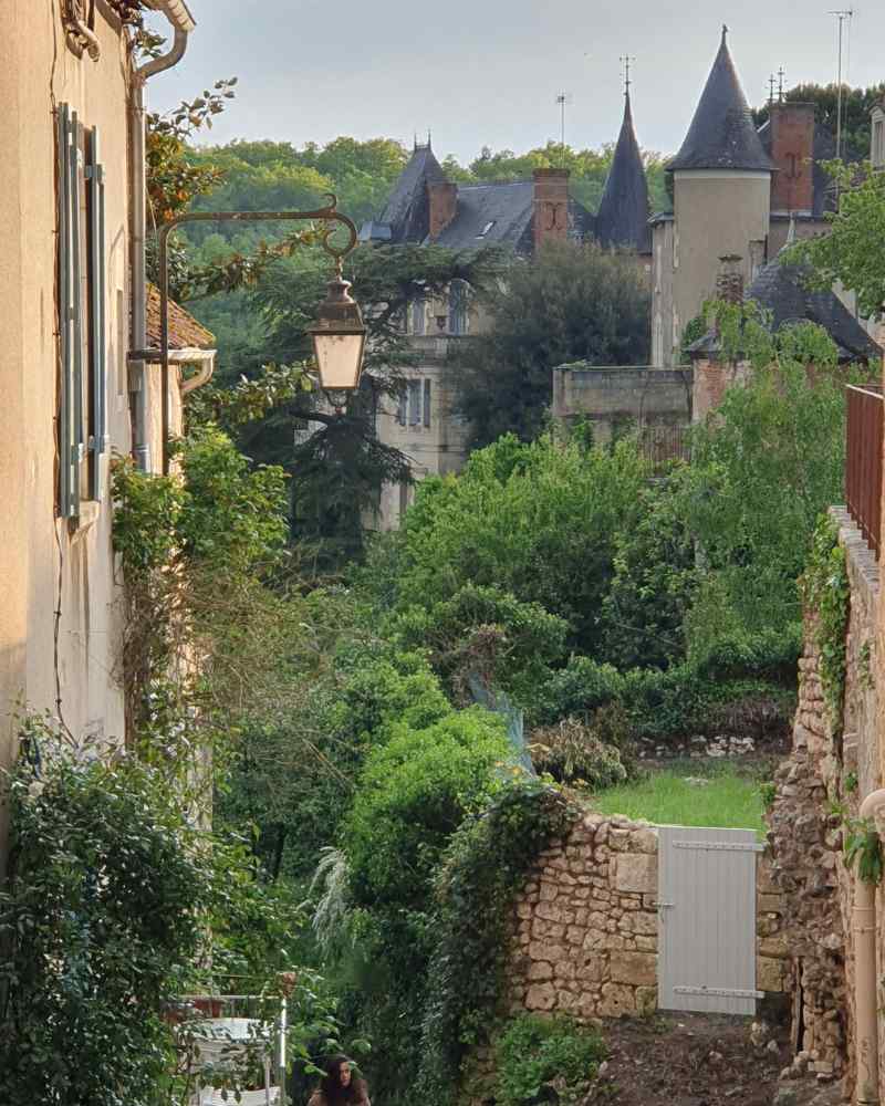 Stone houses and towers seen from a narrow village street surrounded by greenery