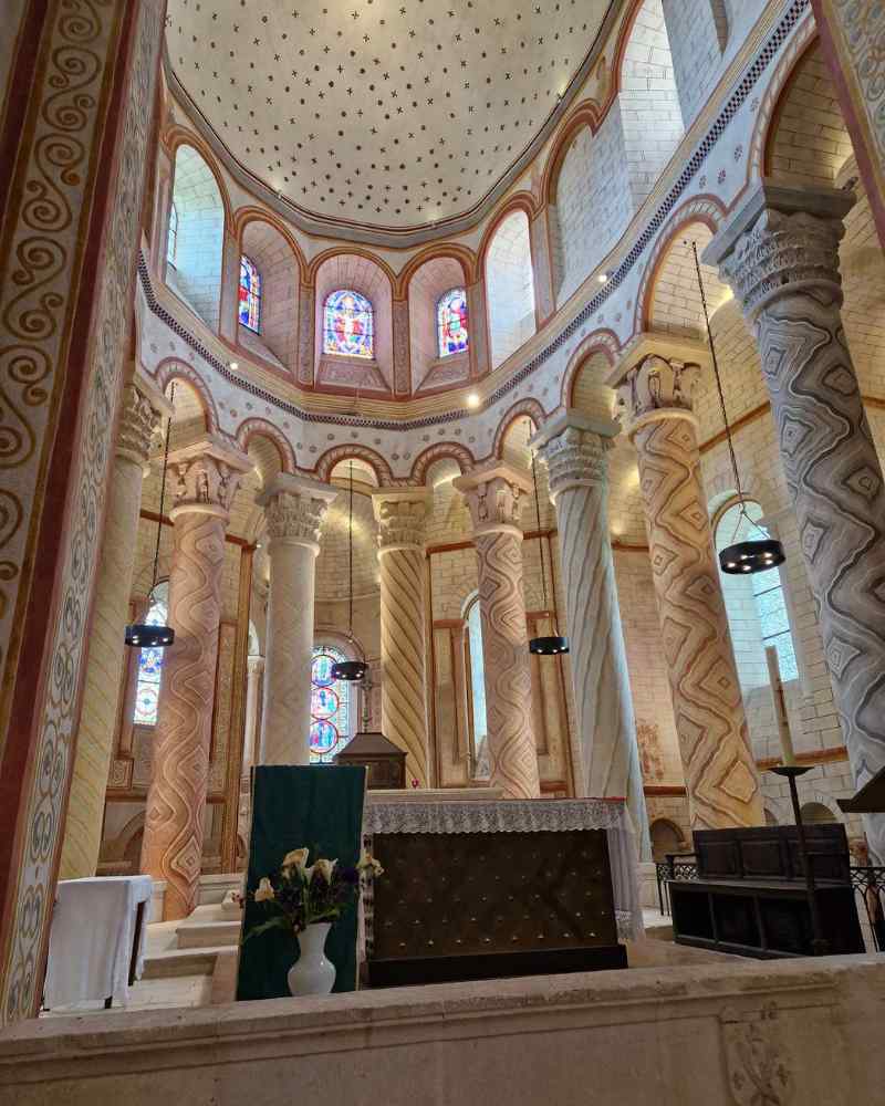Interior of a Romanesque church with carved stone columns, vaulted ceiling and stained-glass windows
