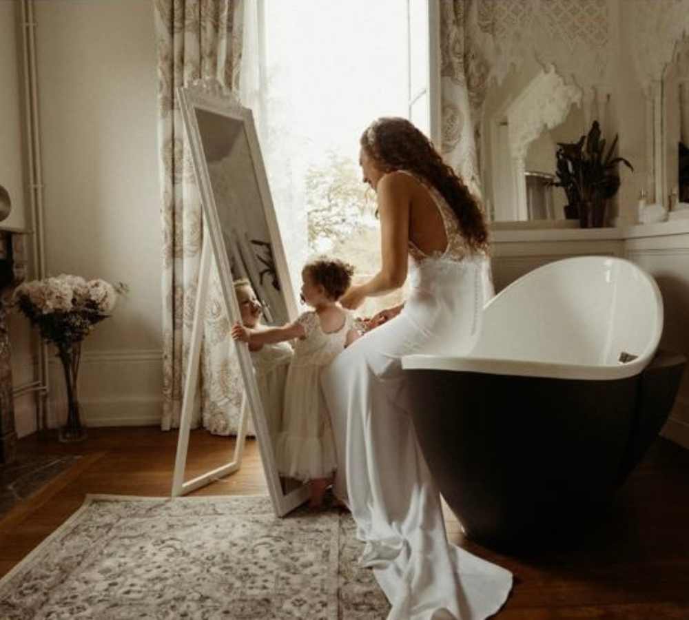 Bride sitting with a young child in a softly lit bathroom suite at Château de la Boutinière, capturing a quiet family moment during a micro wedding venue celebration in France.