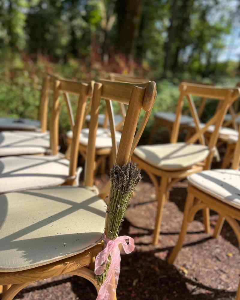 Wooden ceremony chairs decorated with lavender tied in soft pink ribbon, set outdoors at Château de la Boutinière as part of a micro wedding in rural France.