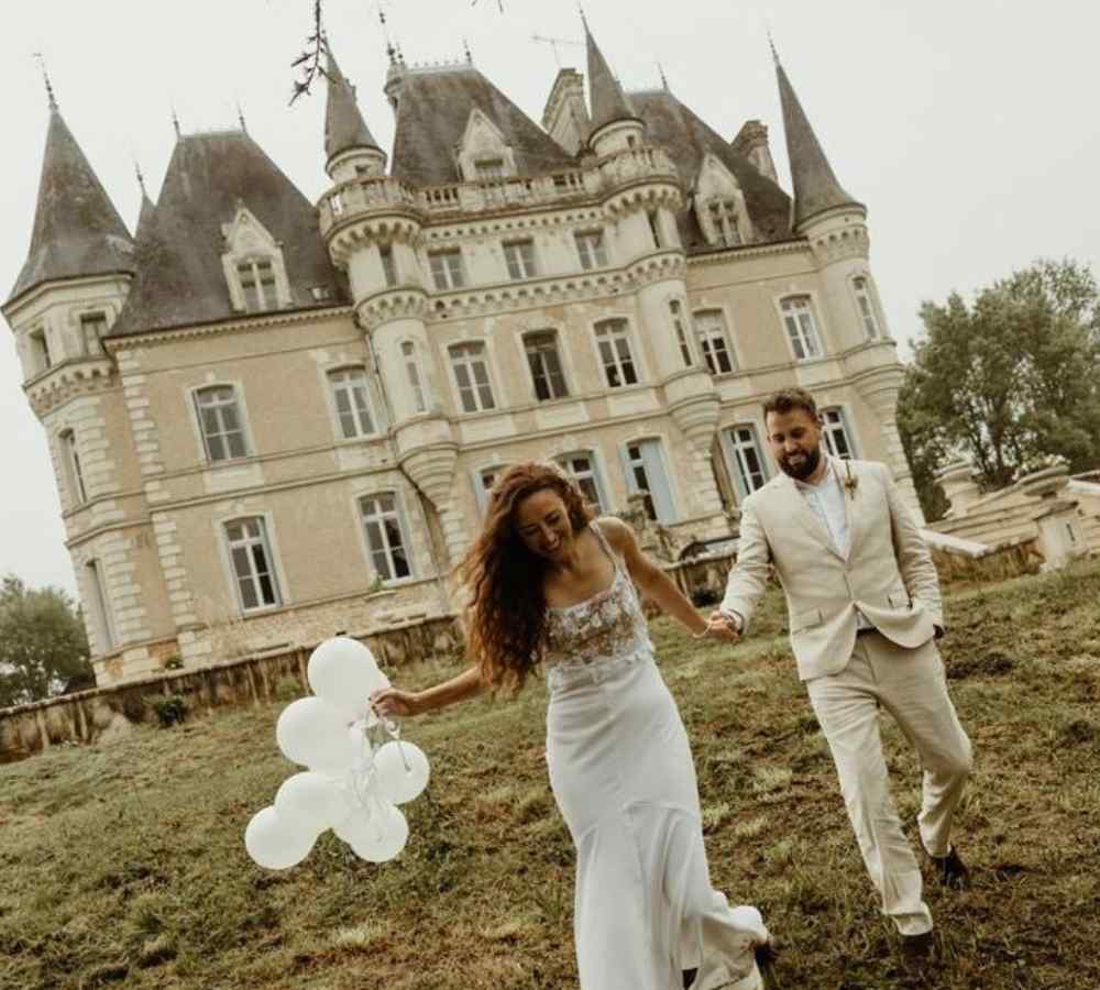 Bride and groom walking hand in hand across the gardens in front of Château de la Boutinière, celebrating their day at an intimate micro wedding venue surrounded by historic château architecture.