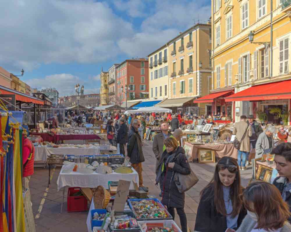 Romantic escapes in France, with a lively local market near Château de la Boutinière featuring colourful stalls, antiques, and visitors browsing in a historic town square.