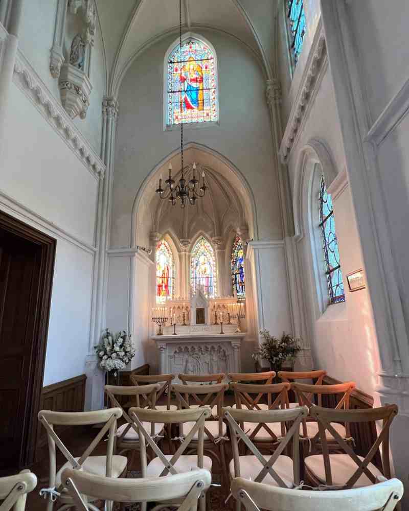 Rows of wooden chairs inside the chapel at Château de la Boutinière facing the altar under a high vaulted ceiling with stained glass windows.