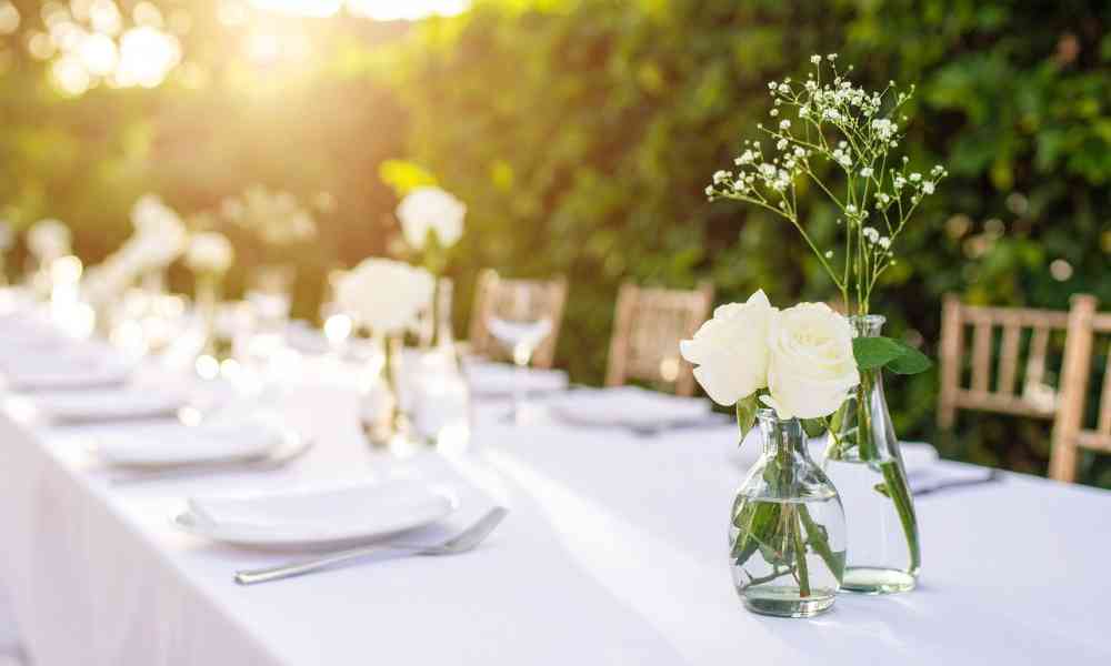 Outdoor dining table with white flowers in glass bottles set for a small celebration at one of the micro wedding venues.
