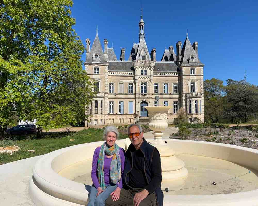 Alison and Zion outside Château de la Boutinière during spring, with the château and fountain behind them.