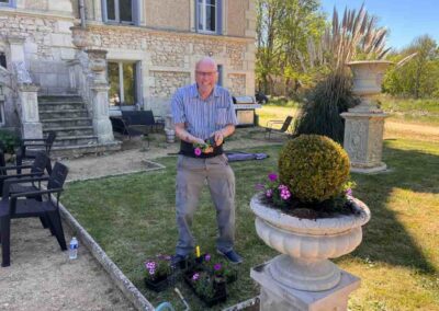 Chateau events gardening day with a guest planting pink flowers into a large stone urn in front of the château.