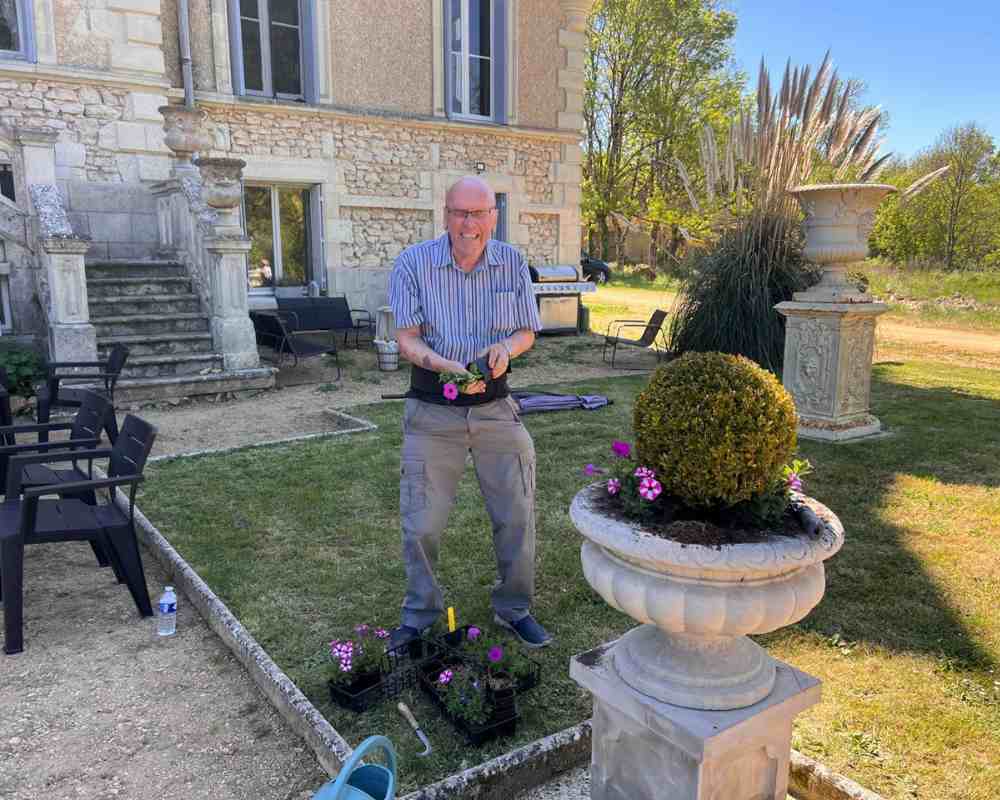 Chateau events gardening day with a guest planting pink flowers into a large stone urn in front of the château.