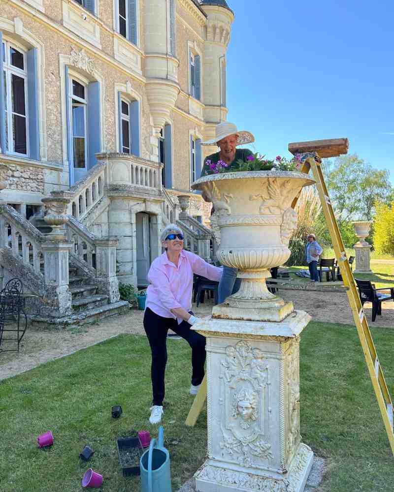 Chateau events gardening day with two women planting flowers into a large stone urn in front of the château.