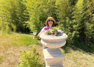 Chateau events gardening day with a smiling woman standing behind a flower-filled stone urn near the bamboo at the château grounds.