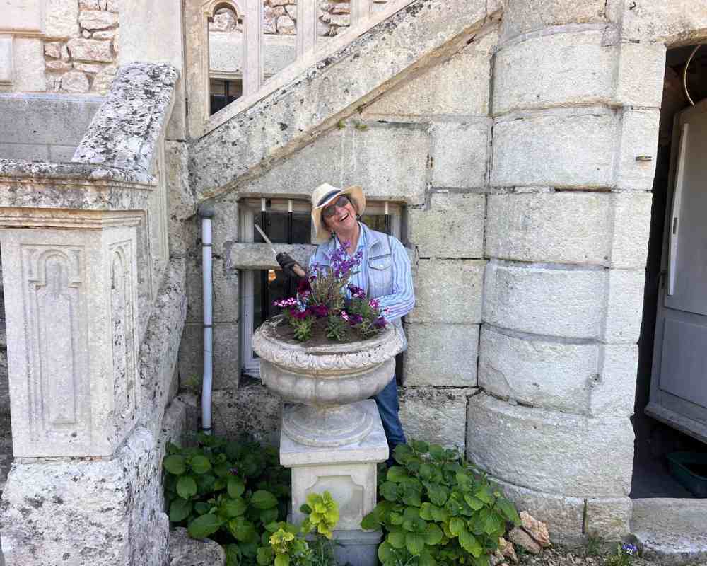 Chateau events gardening day with a smiling guest standing beside a planted stone urn at the château entrance.