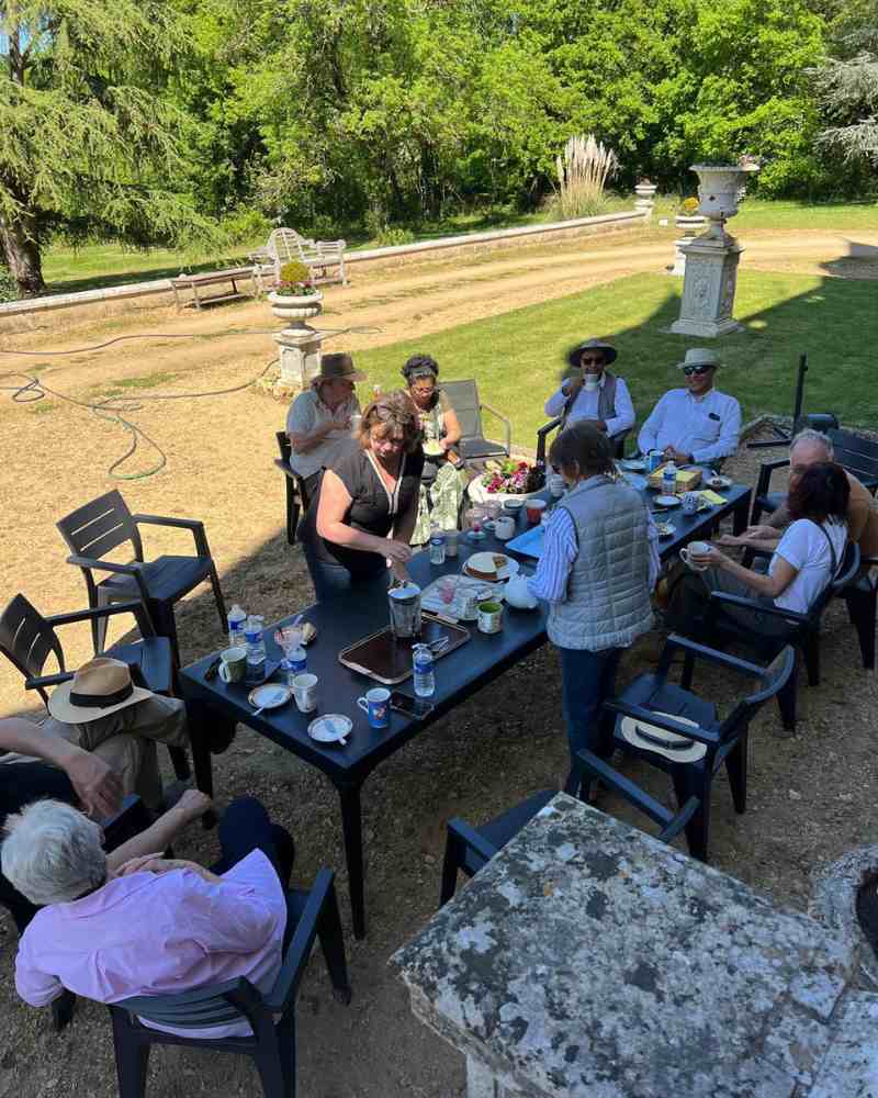 Chateau events gardening day lunch scene with guests seated outdoors beside the château enjoying drinks, cakes and conversation.
