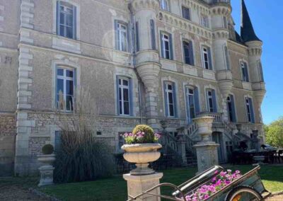 Chateau events gardening day showing a wide view of the château façade with flower-filled urns and a cart planted with pink flowers.