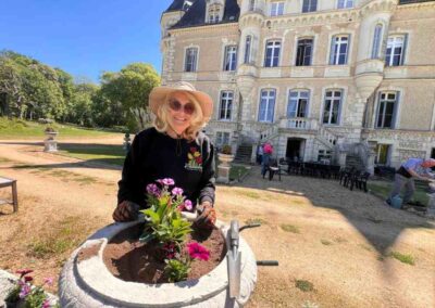 Chateau events gardening day with a woman planting flowers into a large stone urn, with Château de la Boutinière behind her.